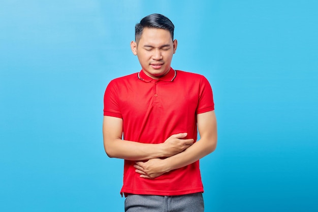 Portrait d'un jeune homme asiatique beau malade souffrant de maux d'estomac problèmes de santé diarrhée inconfort, constipation dans l'intestin isolé sur fond bleu