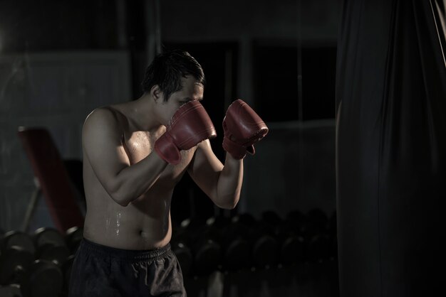 Portrait d&#39;un jeune homme asiatique pratiquant la boxe sur un sac de boxe au gymnase.