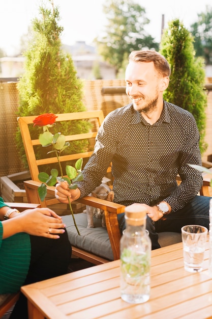 Photo gratuite portrait de jeune homme assis dans un restaurant donnant rose rouge à sa petite amie