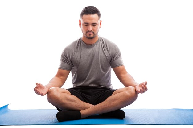 Portrait d'un jeune homme assis sur un tapis de yoga et faisant de la méditation les yeux fermés