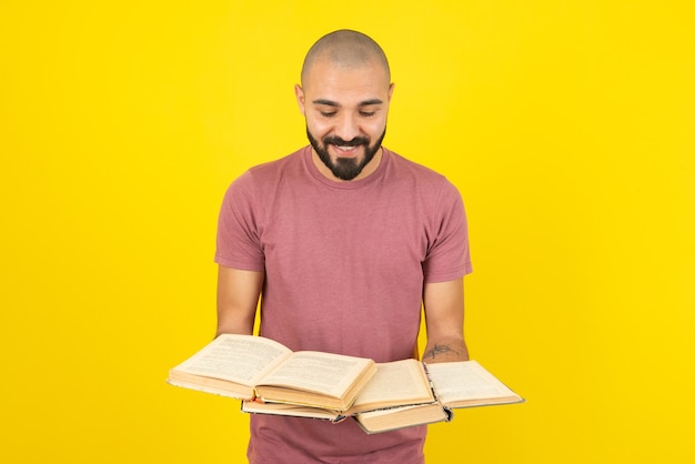 Portrait D'un Jeune Homme Barbu Tenant Des Livres Ouverts Sur Un Mur Jaune.