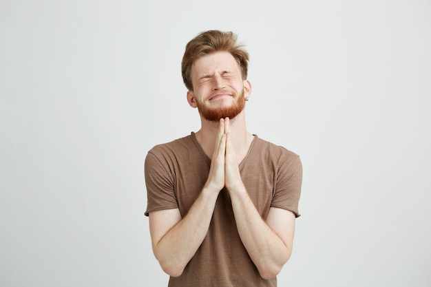 Portrait de jeune homme beau avec barbe priant en espérant.