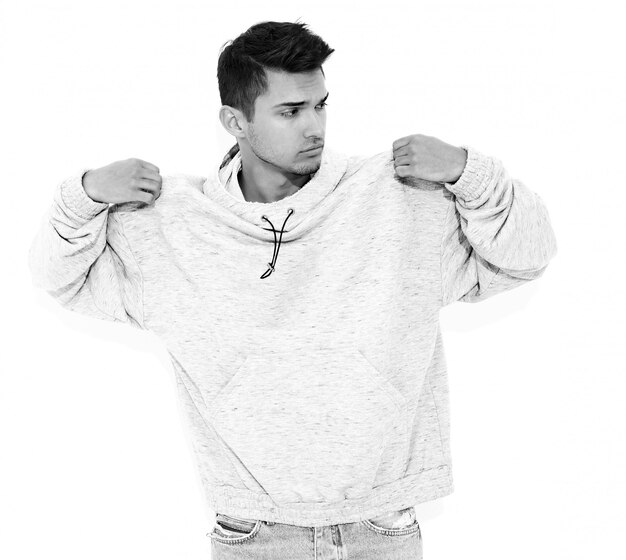 Portrait de jeune homme beau modèle habillé en vêtements à capuche gris décontracté posant sur le mur blanc. Isolé