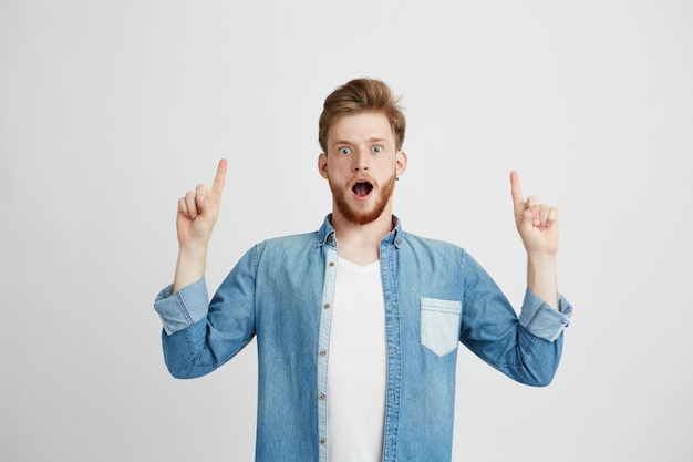 Portrait de jeune homme beau surpris avec la bouche ouverte, pointant le doigt vers le haut.