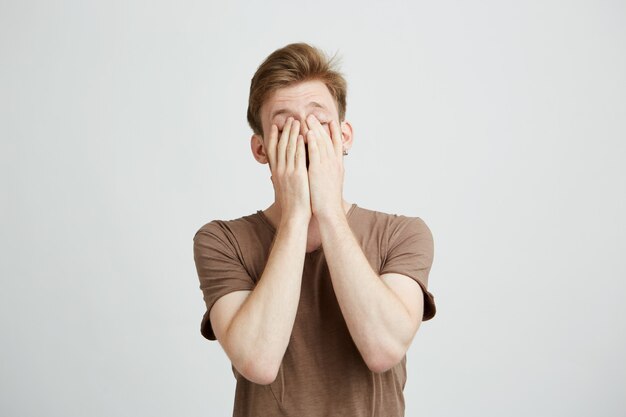 Portrait de jeune homme blond fermant le visage avec les mains.