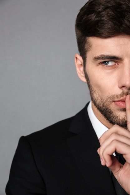 Portrait de jeune homme brune barbu montrant un geste de silence, regardant de côté