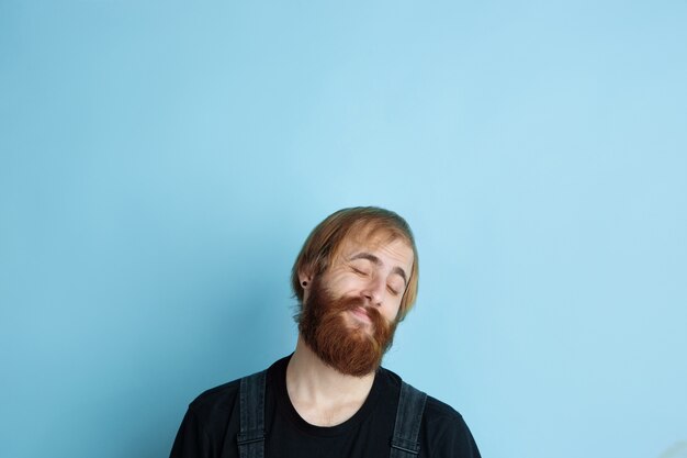 Portrait de jeune homme caucasien a l'air rêveur, mignon et heureux. Recherche et réflexion sur fond de studio bleu. Copyspace pour votre publicité. Concept d'avenir, cible, rêves, visualisation.