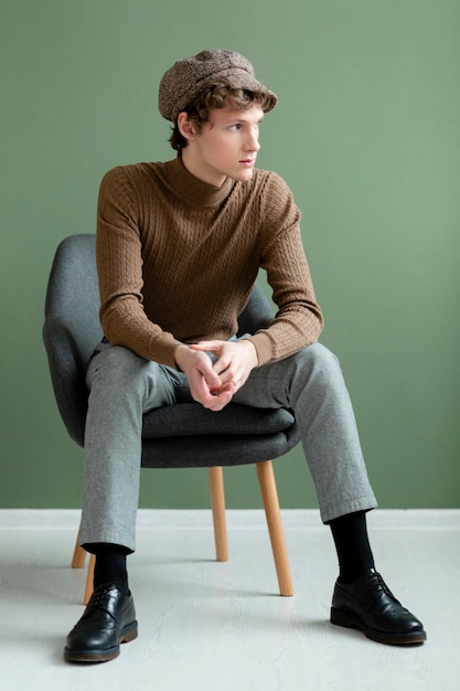 Portrait jeune homme avec chapeau assis sur une chaise