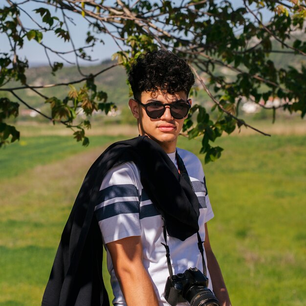 Portrait de jeune homme charmant, lunettes de soleil et appareil photo numérique en regardant la caméra