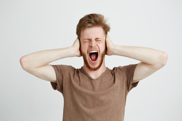 Portrait de jeune homme en colère émotif fermant les oreilles en criant en criant.