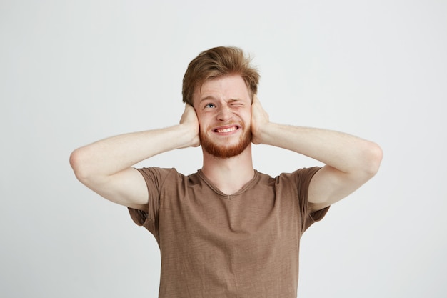 Portrait de jeune homme en colère mécontent avec barbe fermant les oreilles.