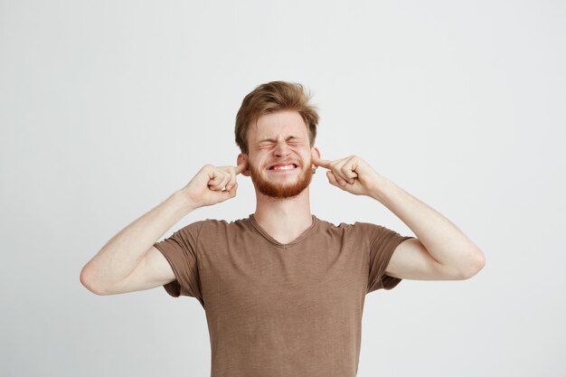 Portrait de jeune homme en colère mécontent avec barbe fermant les oreilles.