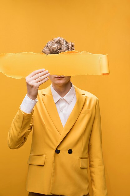 Portrait de jeune homme dans une scène jaune avec du papier déchiré devant le visage