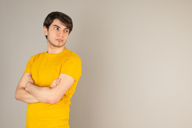 Portrait d'un jeune homme debout avec les bras croisés contre le gris.