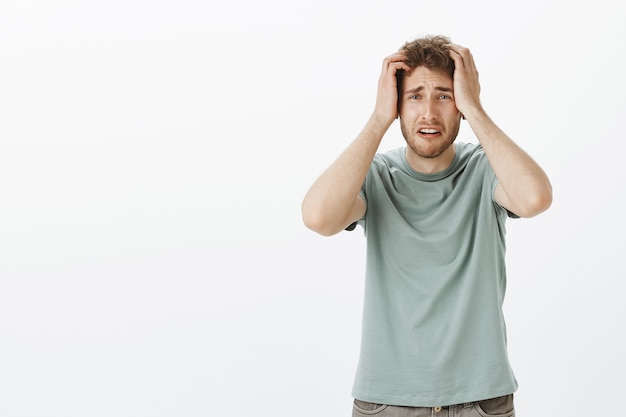 Portrait d'un jeune homme dévasté troublé qui a perdu son emploi, se tenant la main sur la tête et fronçant les sourcils, se sentant inquiet et anxieux en voyant un terrible accident