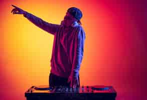 Photo gratuite portrait de jeune homme dj professionnel faisant des sons avec mélangeur isolé sur fond jaune rouge dégradé au néon