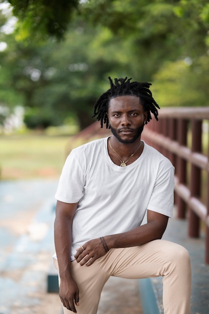 Photo gratuite portrait de jeune homme avec des dreadlocks afro et un t-shirt blanc à l'extérieur