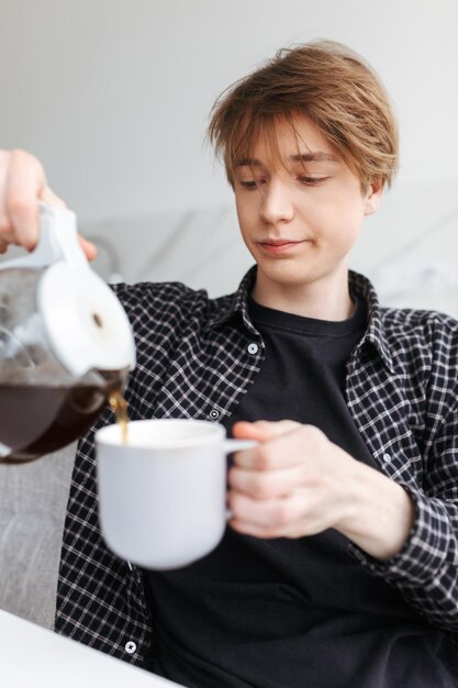 Portrait de jeune homme endormi assis et versant du café dans la cuisine à la maison