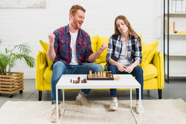 Portrait d&#39;un jeune homme excité assis avec sa petite amie triste jouant aux échecs