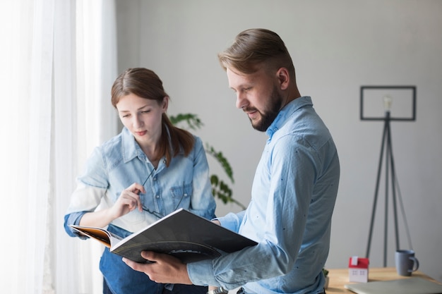 Portrait de jeune homme et femme à la recherche d&#39;un catalogue intérieur au bureau