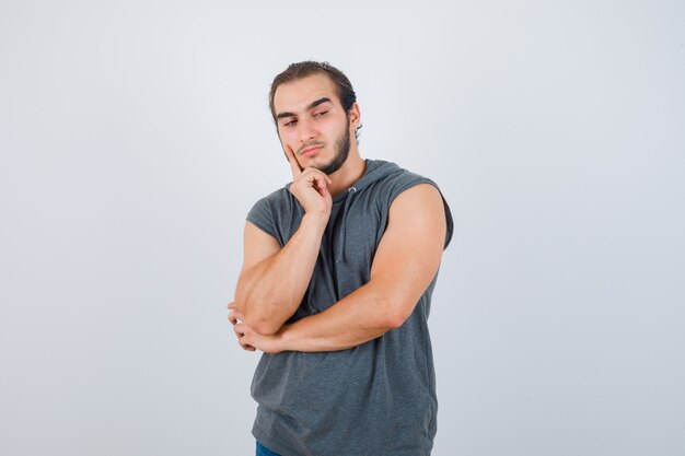 Portrait de jeune homme fit en gardant le doigt sur la joue en sweat à capuche sans manches et à la vue de face pensive