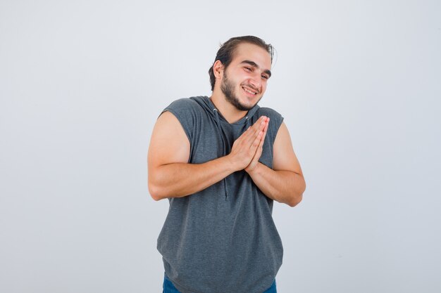 Photo gratuite portrait de jeune homme fit main dans la main en signe de prière en sweat à capuche sans manches et à la vue de face reconnaissante