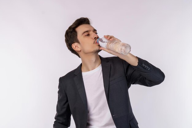 Portrait d'un jeune homme heureux buvant de l'eau d'une bouteille et regardant la caméra isolée sur fond blanc