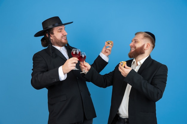 Photo gratuite portrait d'un jeune homme juif orthodoxe isolé sur mur bleu studio rencontre la pâque manger les oreilles de l'amans avec du vin