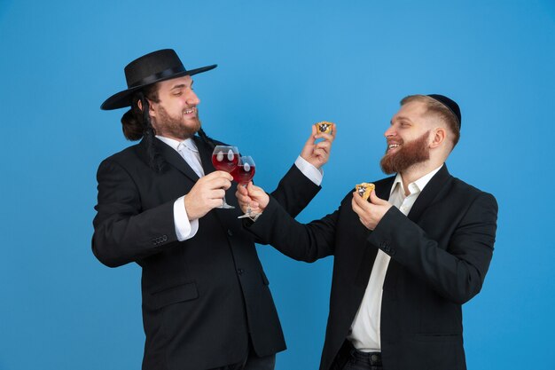 Portrait d'un jeune homme juif orthodoxe isolé sur mur bleu studio rencontre la Pâque manger les oreilles de l'amans avec du vin