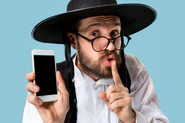 Portrait d'un jeune homme juif orthodoxe avec téléphone mobile au studio