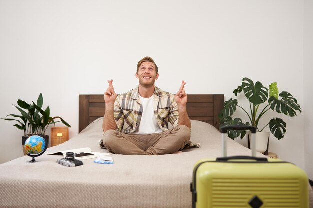 Photo gratuite portrait d'un jeune homme méditant sur un lit après avoir emballé sa valise pour les vacances d'été assis avec