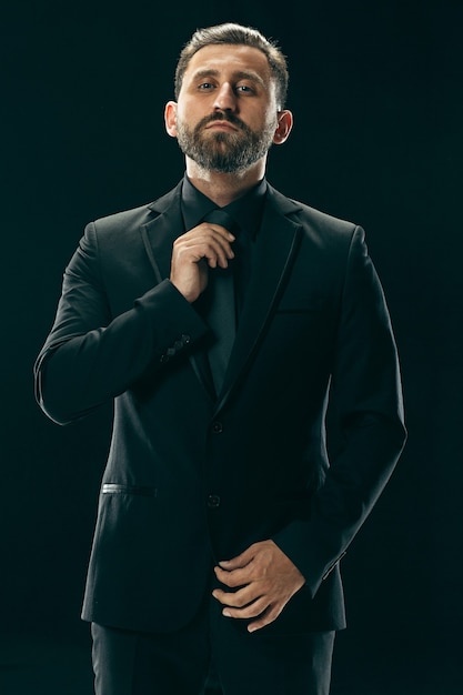 Portrait d'un jeune homme à la mode avec une coupe de cheveux élégante portant un costume tendance posant sur fond noir.