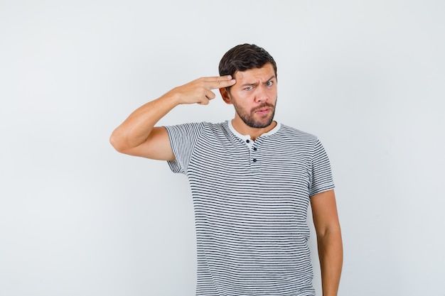 Portrait de jeune homme montrant un geste de suicide en t-shirt et regardant une vue de face sérieuse