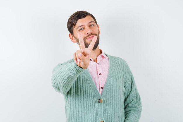 Portrait de jeune homme montrant V-sign en chemise, cardigan et à la vue de face joyeuse