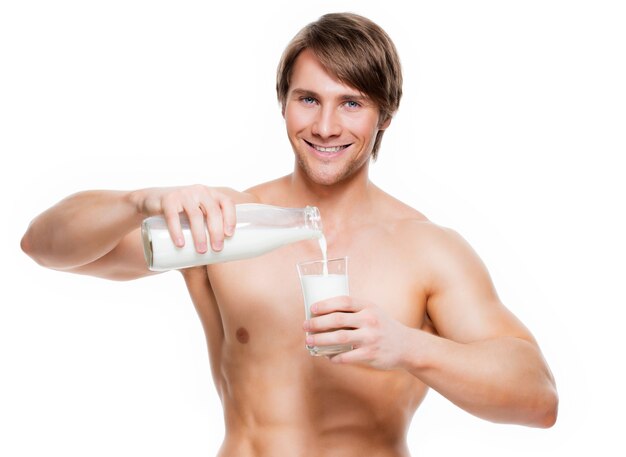 Portrait d'un jeune homme musclé beau verser du lait dans un verre - isolé sur un mur blanc.