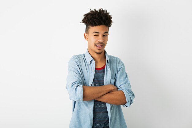 Portrait de jeune homme noir hipster posant sur fond de mur de studio blanc isolé, tenue élégante, coiffure afro drôle, clin de œil, grimace