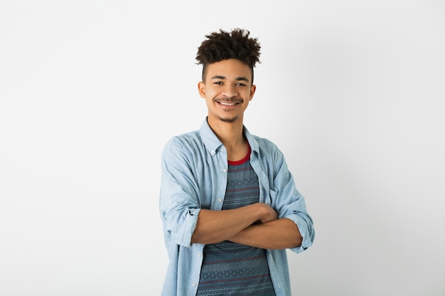 Portrait de jeune homme noir hipster posant sur fond de mur de studio blanc isolé, tenue élégante, coiffure afro drôle, souriant, heureux, confiant, les bras croisés sur la poitrine