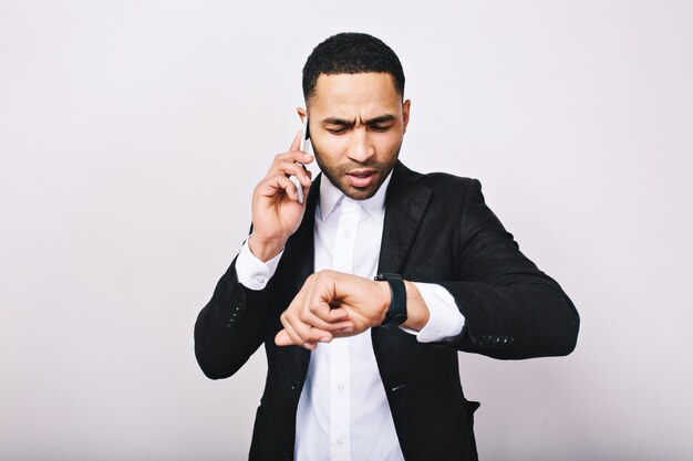 Portrait jeune homme occupé en chemise blanche, veste noire parlant au téléphone et regardant la montre. Homme d'affaires élégant, occupé, temps de travail, réunion, entreprise moderne.