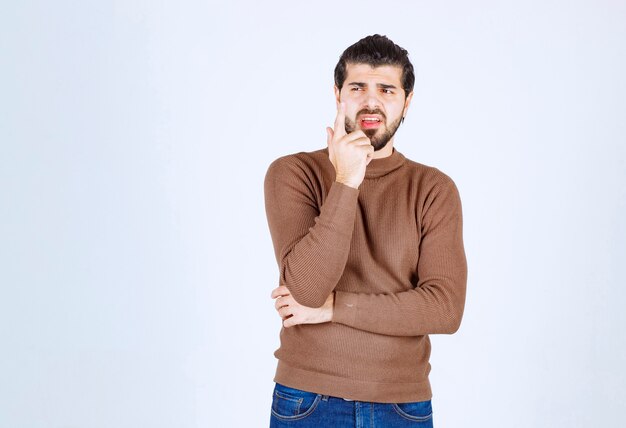 Portrait d'un jeune homme pensant et debout contre un mur blanc.