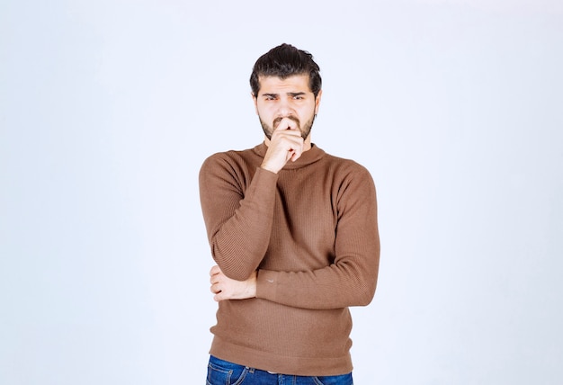 Portrait d'un jeune homme pensant et debout contre un mur blanc.