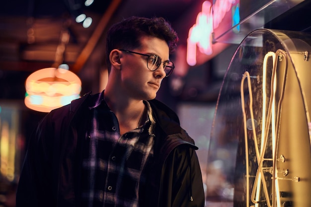 Portrait d'un jeune homme pensif portant un sweat à capuche de sport regardant l'enseigne lumineuse dans la rue la nuit.