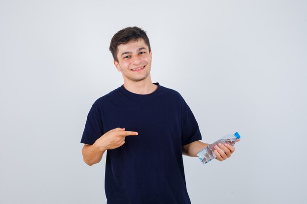 Portrait de jeune homme pointant sur une bouteille d'eau en t-shirt noir et à la vue de face confiante