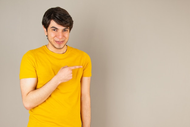 Portrait d'un jeune homme pointant du doigt avec les doigts contre le gris.