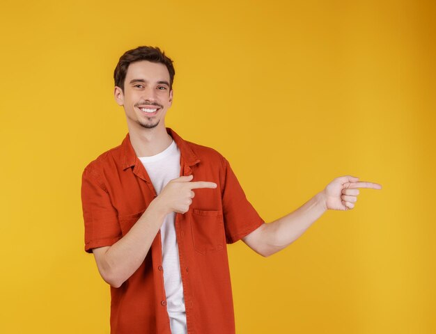 Portrait de jeune homme pointant du doigt l'espace de copie isolé sur fond de studio jaune