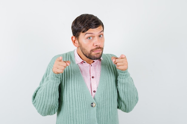 Portrait de jeune homme pointant vers l'avant en chemise, cardigan et à la vue de face perplexe