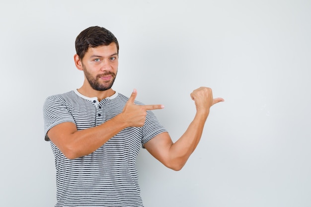 Portrait de jeune homme pointant vers la droite en t-shirt rayé et à la vue de face confiant