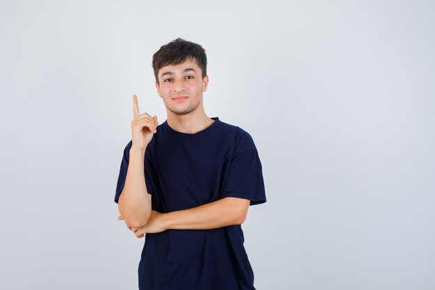 Portrait de jeune homme pointant vers le haut en t-shirt noir et à la vue de face confiante