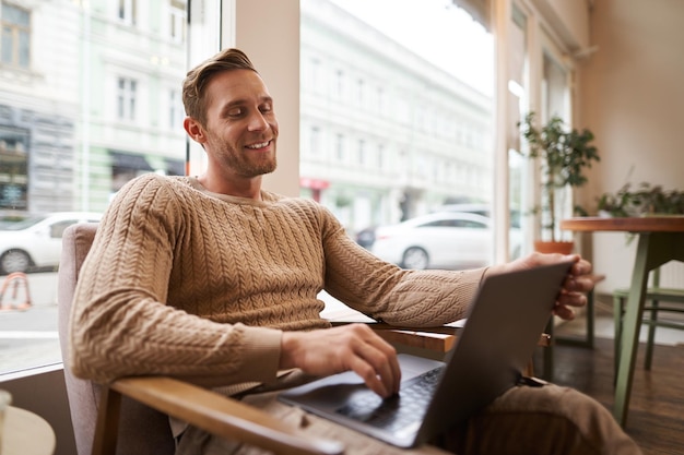 Portrait d'un jeune homme professionnel assis dans un café avec un ordinateur portable buvant du café et travaillant