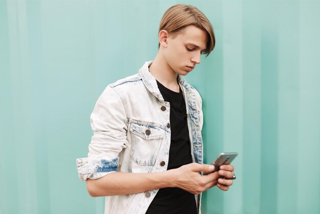 Portrait d'un jeune homme réfléchi debout et utilisant son téléphone portable sur fond bleu