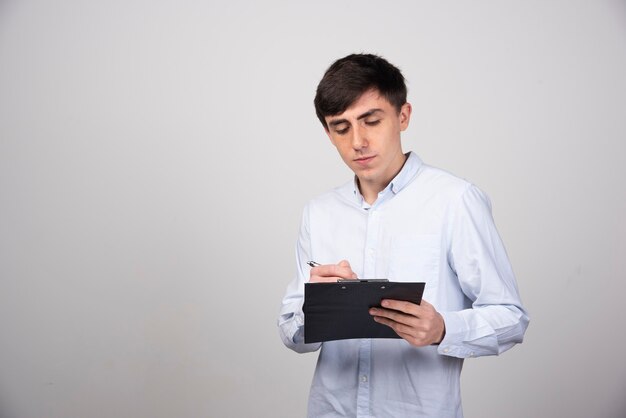 Portrait de jeune homme regardant le presse-papiers sur le mur gris.